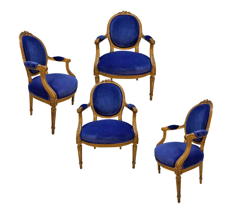 A set of four Louis XVI style armchairs featuring carved giltwood frames with oval medallion backs and royal blue velvet upholstery.