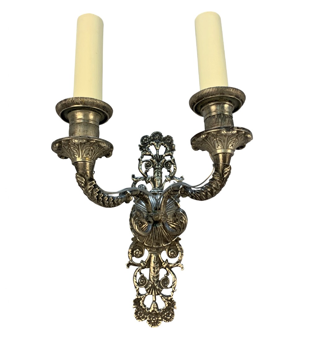 A pair of silver-plated French Empire style two-light wall sconces with ornate foliate backplates and cream candle sleeves. View V
