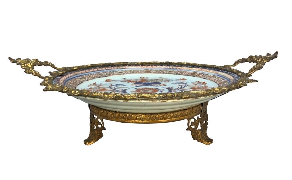 A circular Chinese Imari porcelain plate decorated with blue and red floral patterns, set within a gilt bronze ormolu frame with foliage handles. View II