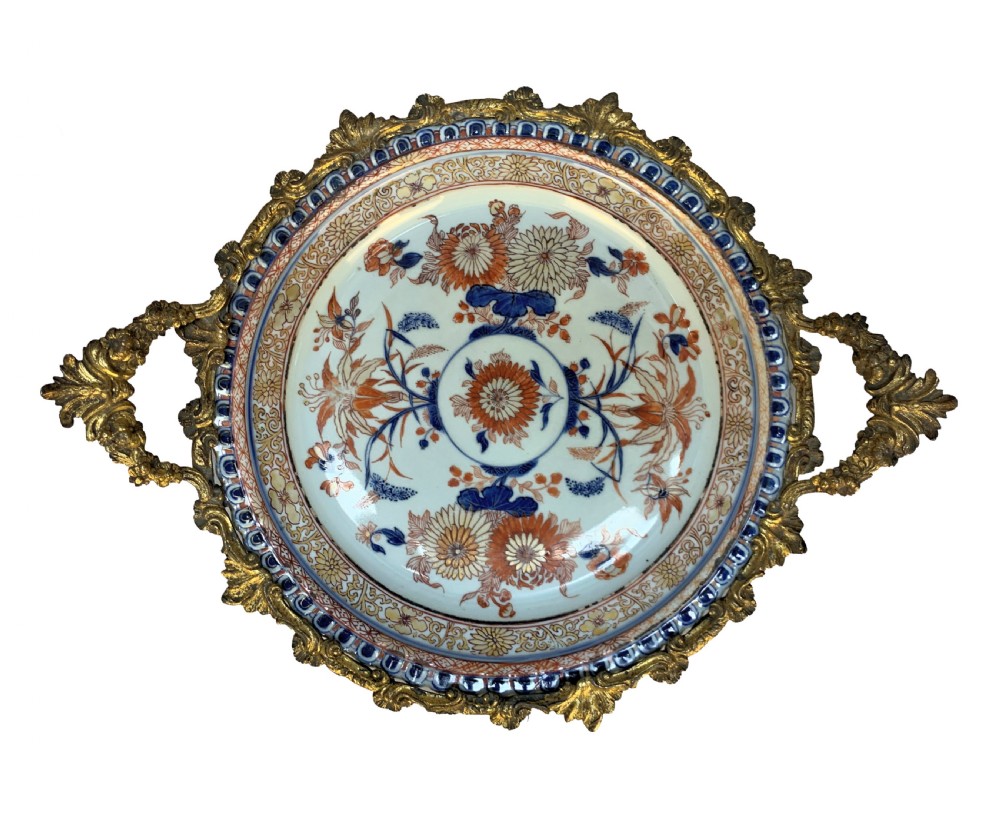 A circular Chinese Imari porcelain plate decorated with blue and red floral patterns, set within a gilt bronze ormolu frame with foliage handles. View III