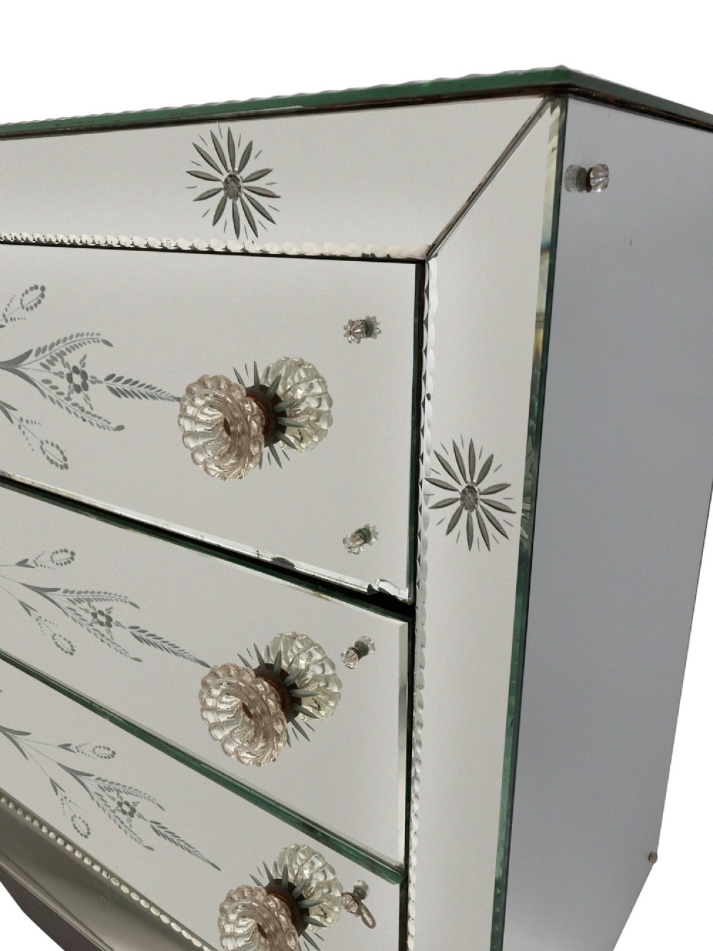 A 1930s French Art Deco three-drawer chest clad entirely in etched mirrored glass with starburst corner motifs and a black wooden base. View III