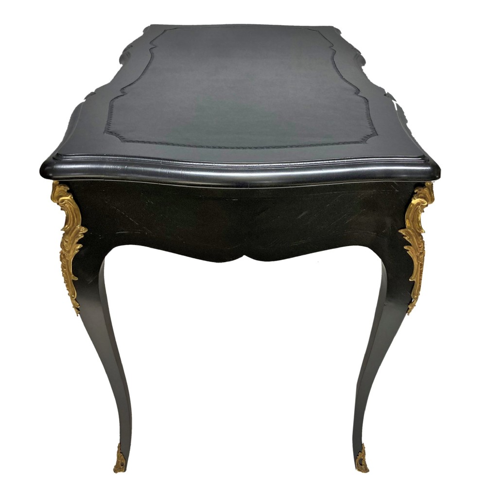 A black lacquered Louis XV style writing table featuring a serpentine top with a leather writing surface, decorative gilt bronze mounts, three frieze drawers, and cabriole legs with gilded sabots. View VI