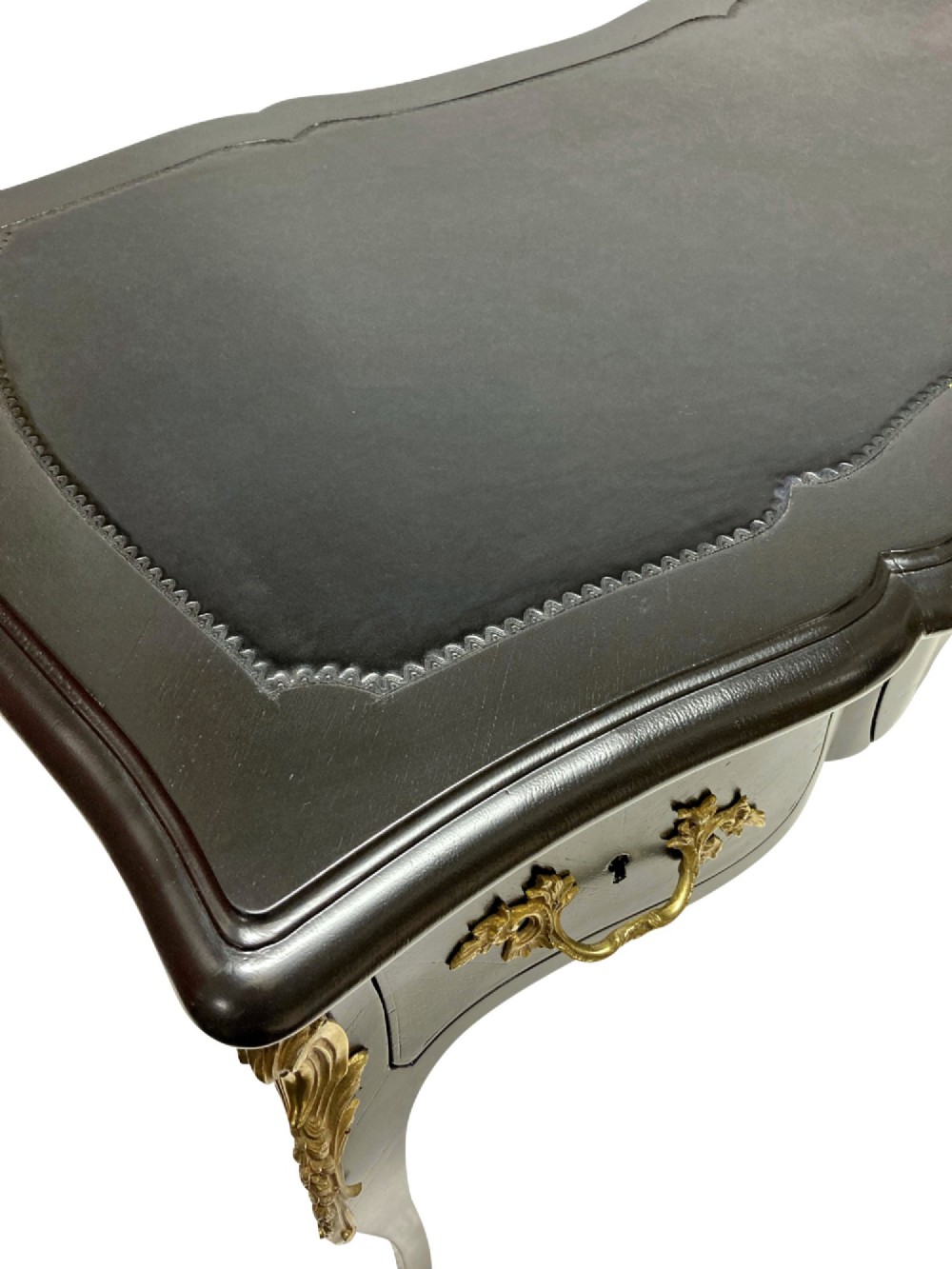 A black lacquered Louis XV style writing table featuring a serpentine top with a leather writing surface, decorative gilt bronze mounts, three frieze drawers, and cabriole legs with gilded sabots. View VII