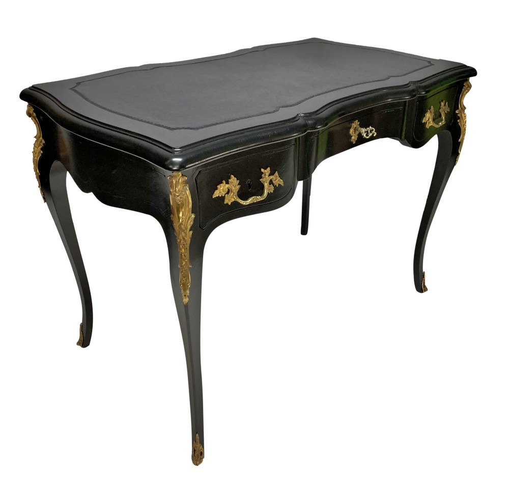 A black lacquered Louis XV style writing table featuring a serpentine top with a leather writing surface, decorative gilt bronze mounts, three frieze drawers, and cabriole legs with gilded sabots. View VIII