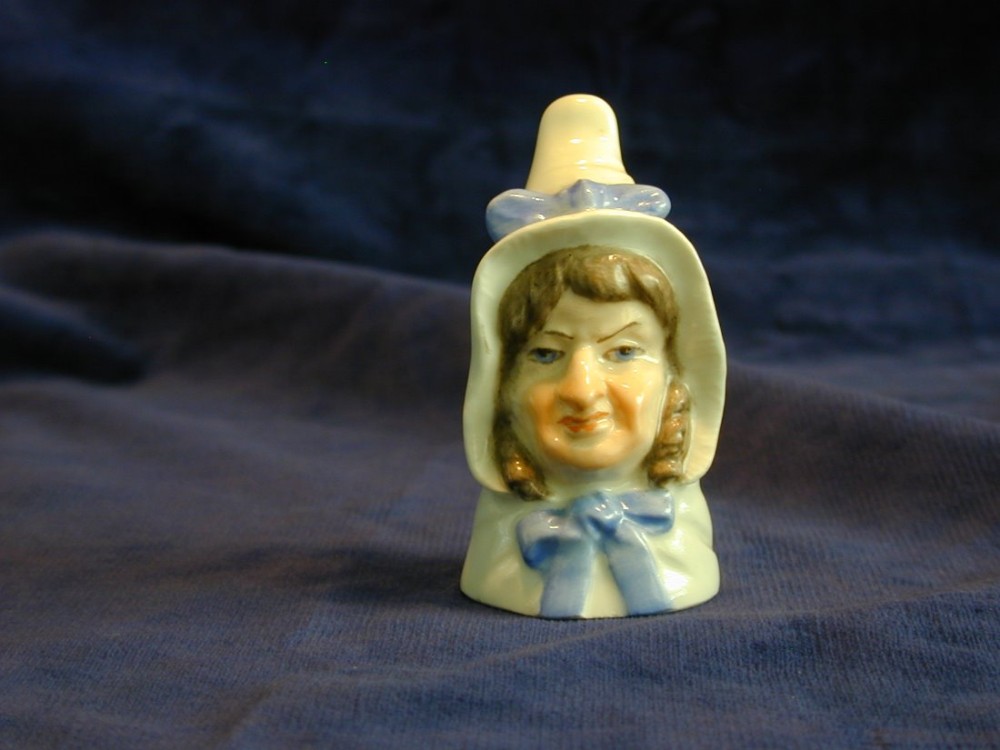 A small Royal Worcester porcelain candle snuffer shaped as the head of Mrs Caudle wearing a bonnet tied with a blue bow.