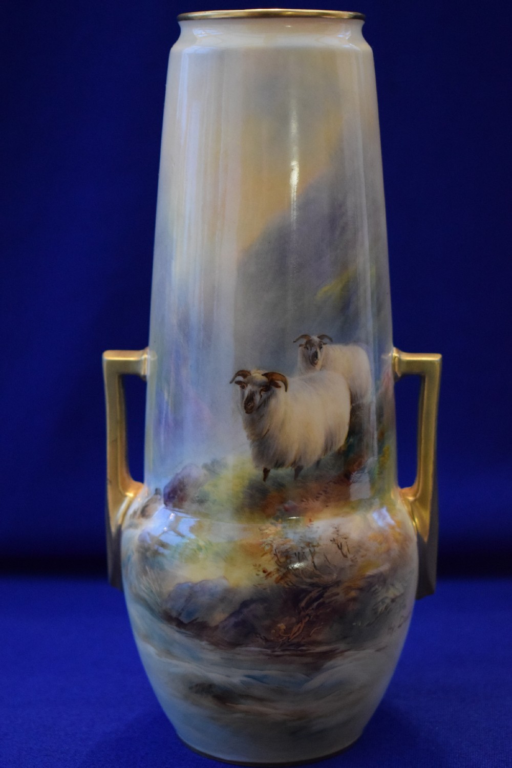 A tall, tapered antique Royal Worcester porcelain vase featuring a hand-painted scene of two sheep in a misty highland landscape with gilded angular side handles.
