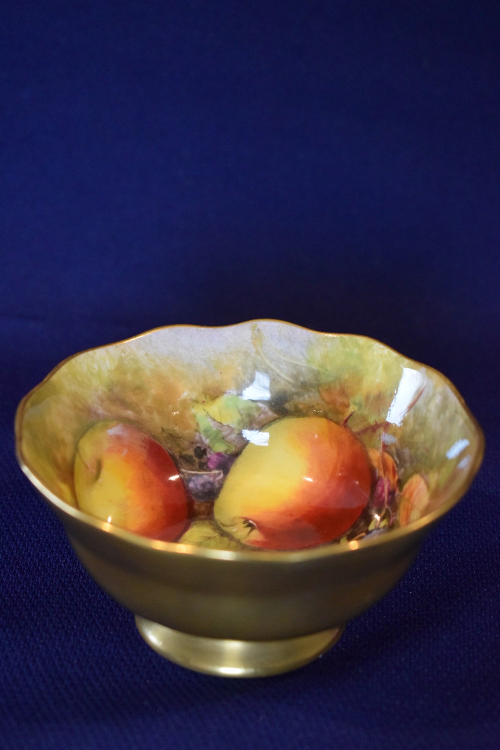 A small gilt porcelain sugar bowl with a scalloped edge featuring a hand-painted fruit motif on the interior surface.