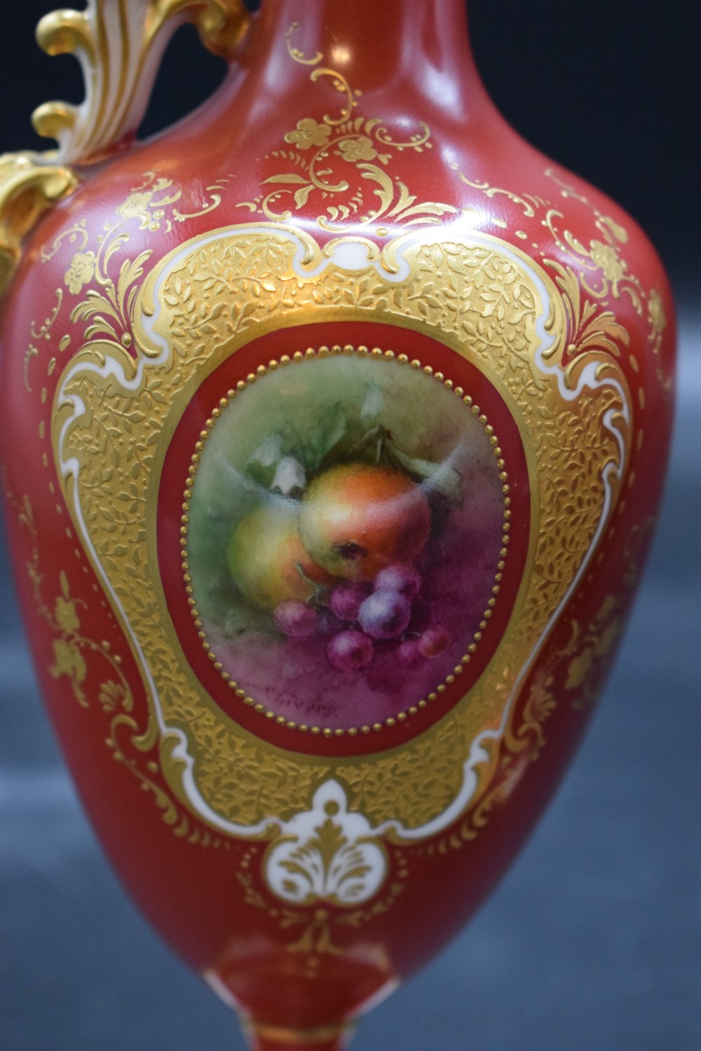 A pair of crimson red porcelain ewers featuring hand-painted fruit vignettes enclosed within gilt scrollwork borders and loop handles on square pedestal bases. View IV