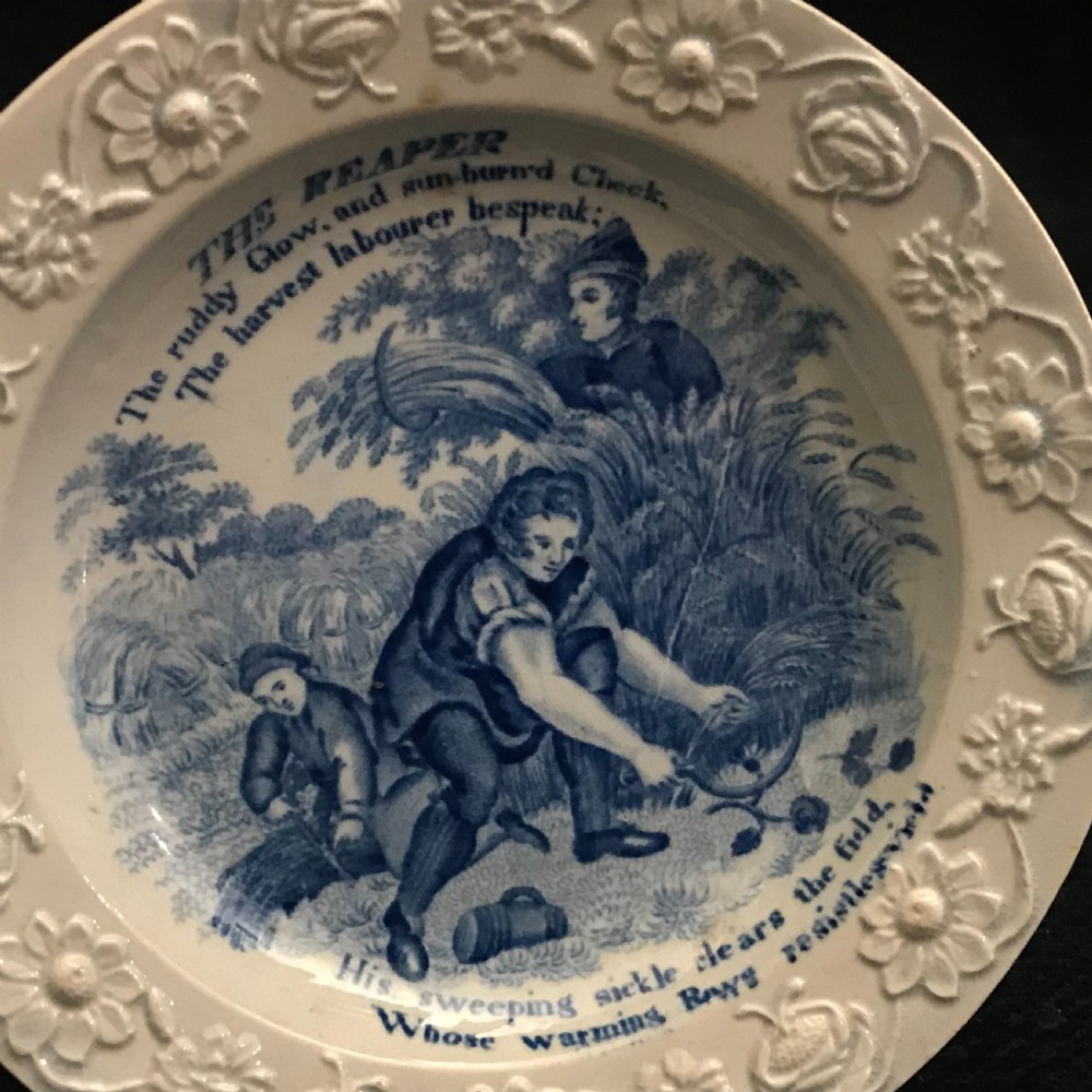 A set of four circular cream pearlware nursery plates featuring blue transfer-printed scenes of historical trades enclosed by moulded floral borders. View III