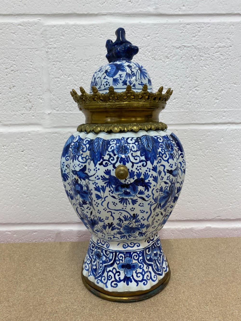 A blue and white floral patterned ceramic vase clock with a fitted lid, featuring an integrated brass clock face with Roman numerals. View III