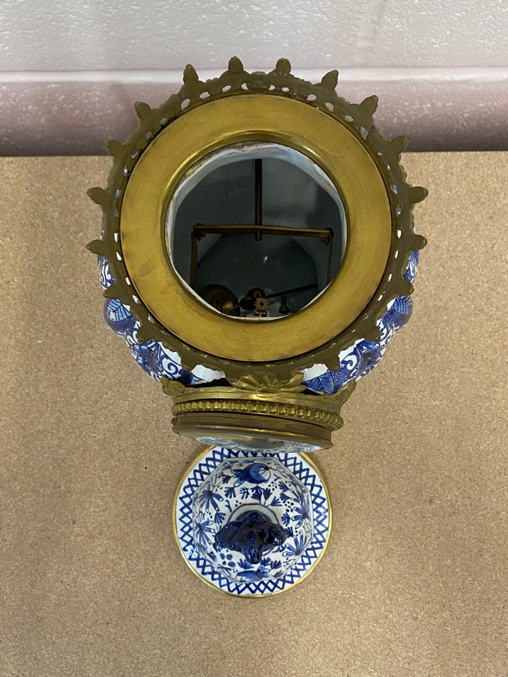 A blue and white floral patterned ceramic vase clock with a fitted lid, featuring an integrated brass clock face with Roman numerals. View IV