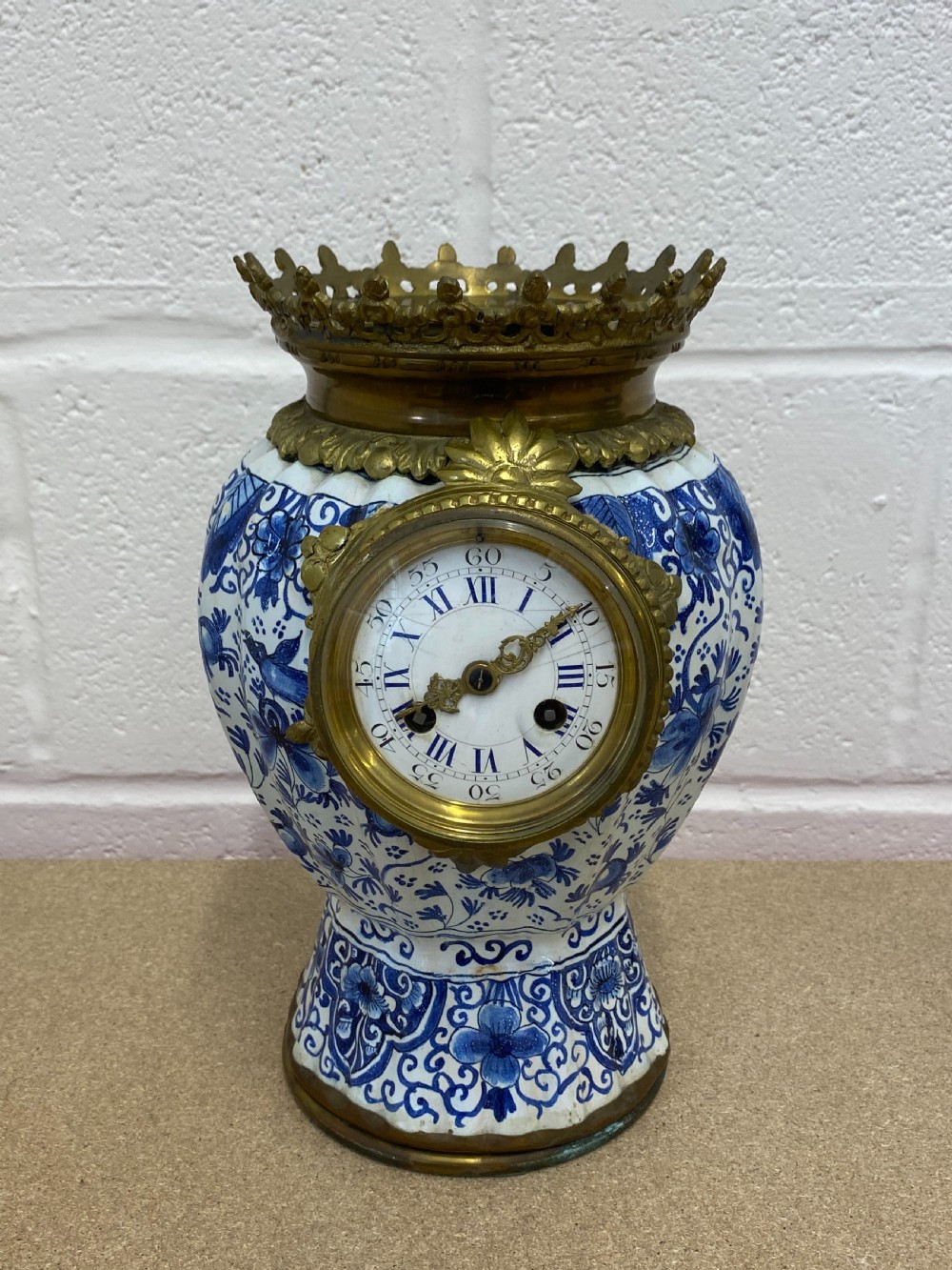 A blue and white floral patterned ceramic vase clock with a fitted lid, featuring an integrated brass clock face with Roman numerals. View V