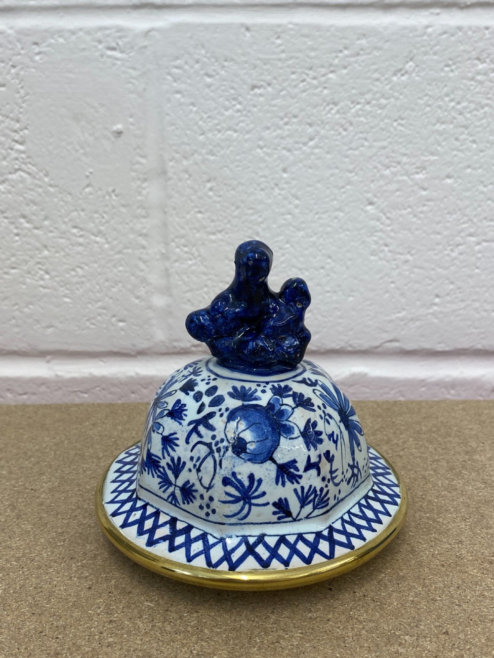 A blue and white floral patterned ceramic vase clock with a fitted lid, featuring an integrated brass clock face with Roman numerals. View VI