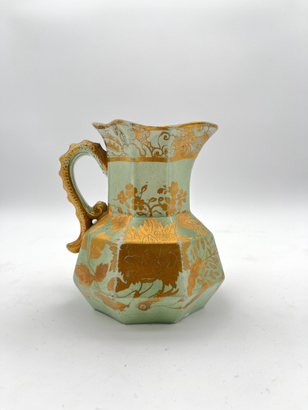 A set of three graduated octagonal sage green ironstone jugs decorated with gilded floral motifs and ornate moulded scroll handles. View III