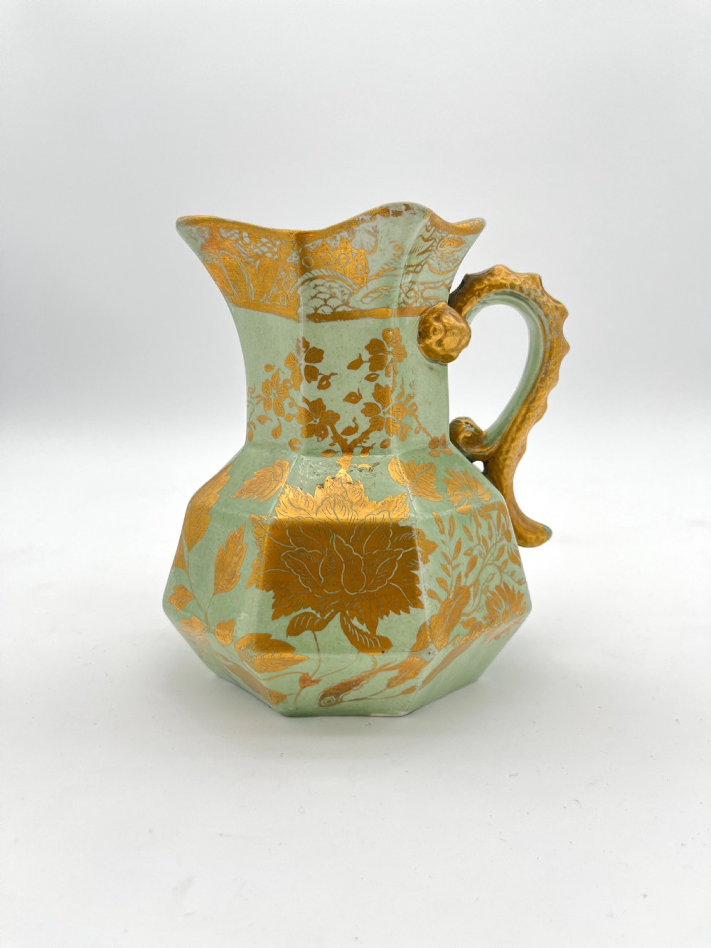 A set of three graduated octagonal sage green ironstone jugs decorated with gilded floral motifs and ornate moulded scroll handles. View VI