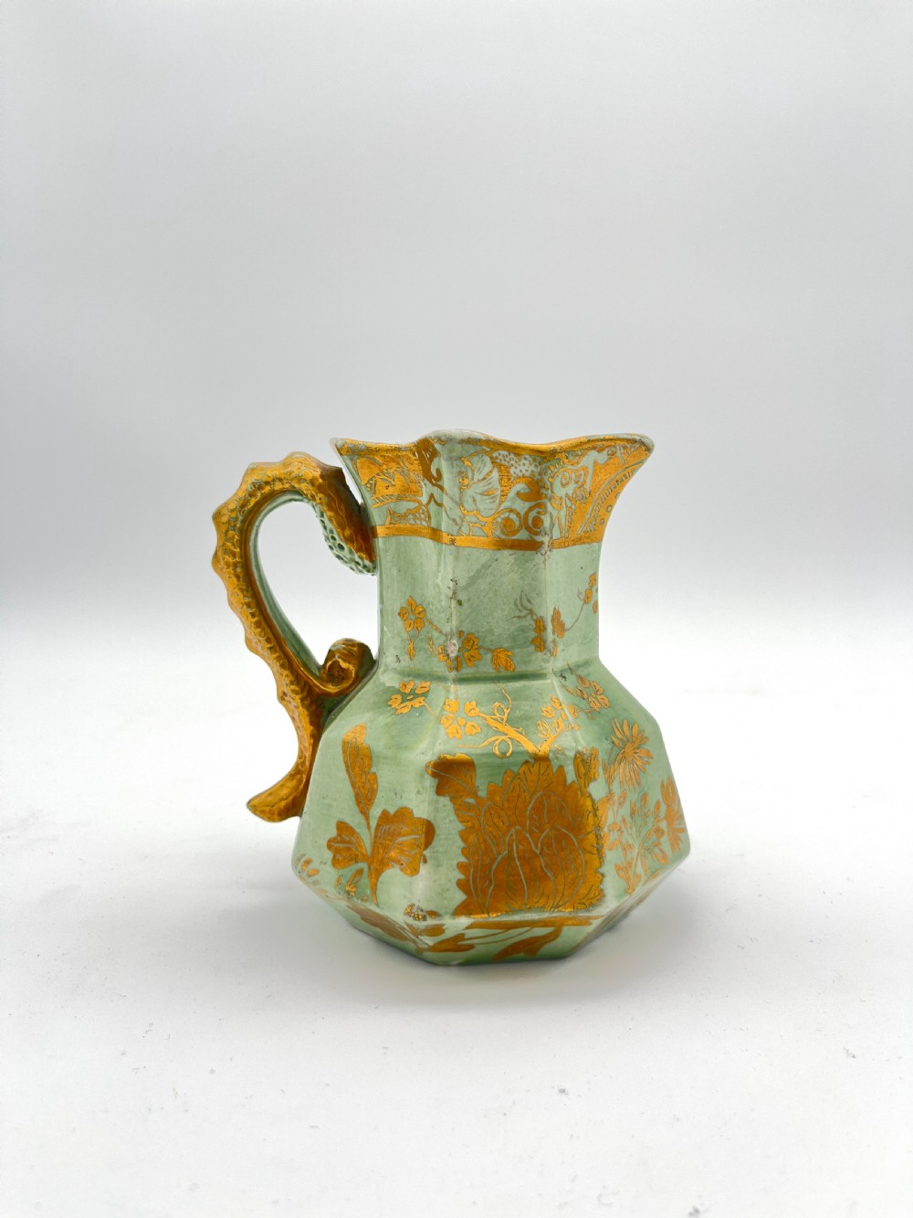 A set of three graduated octagonal sage green ironstone jugs decorated with gilded floral motifs and ornate moulded scroll handles. View X