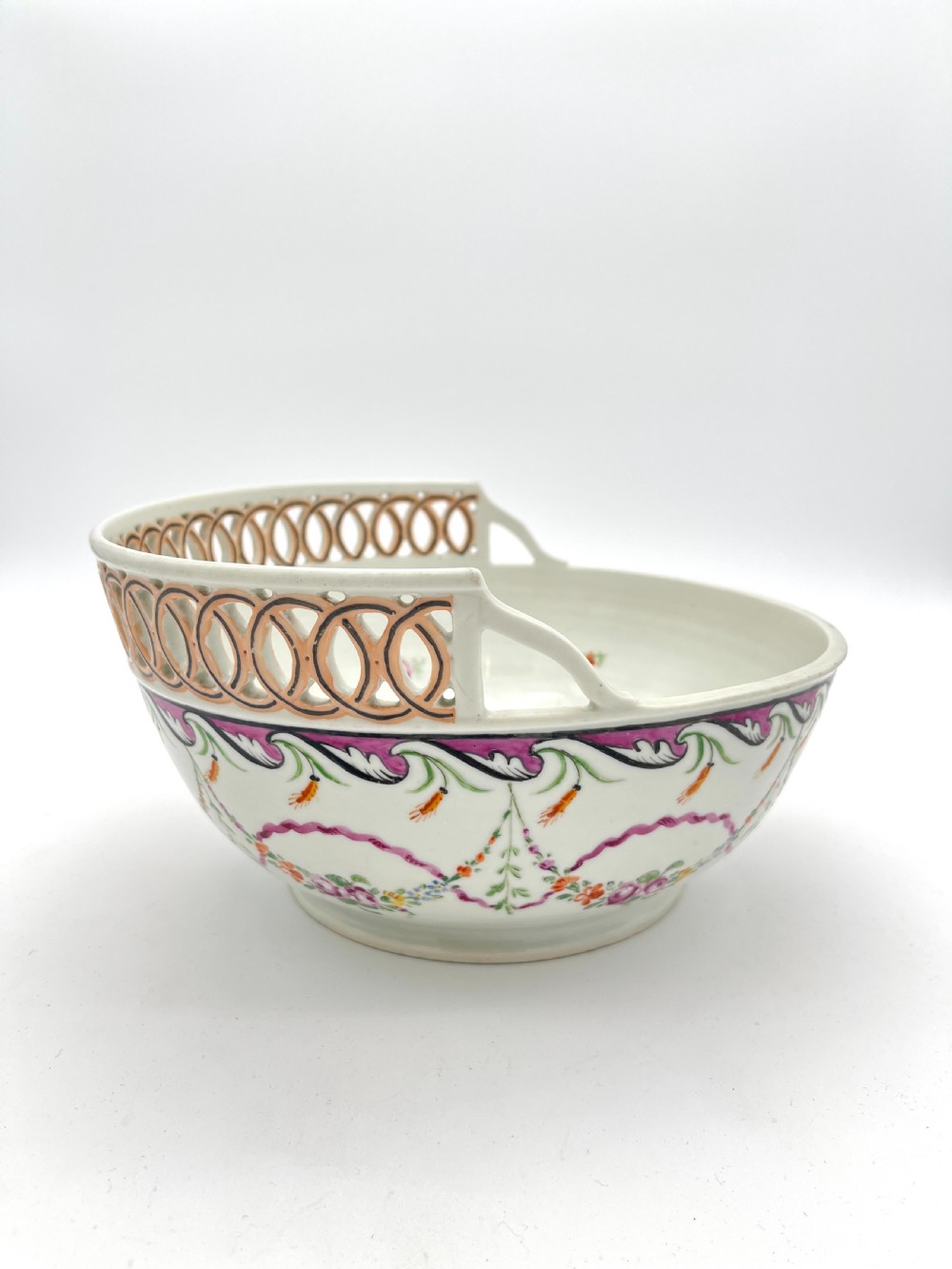 An eighteenth-century white porcelain punch bowl featuring a half-pierced reticulated gallery rim and hand-painted floral swags in pink, orange, and green.