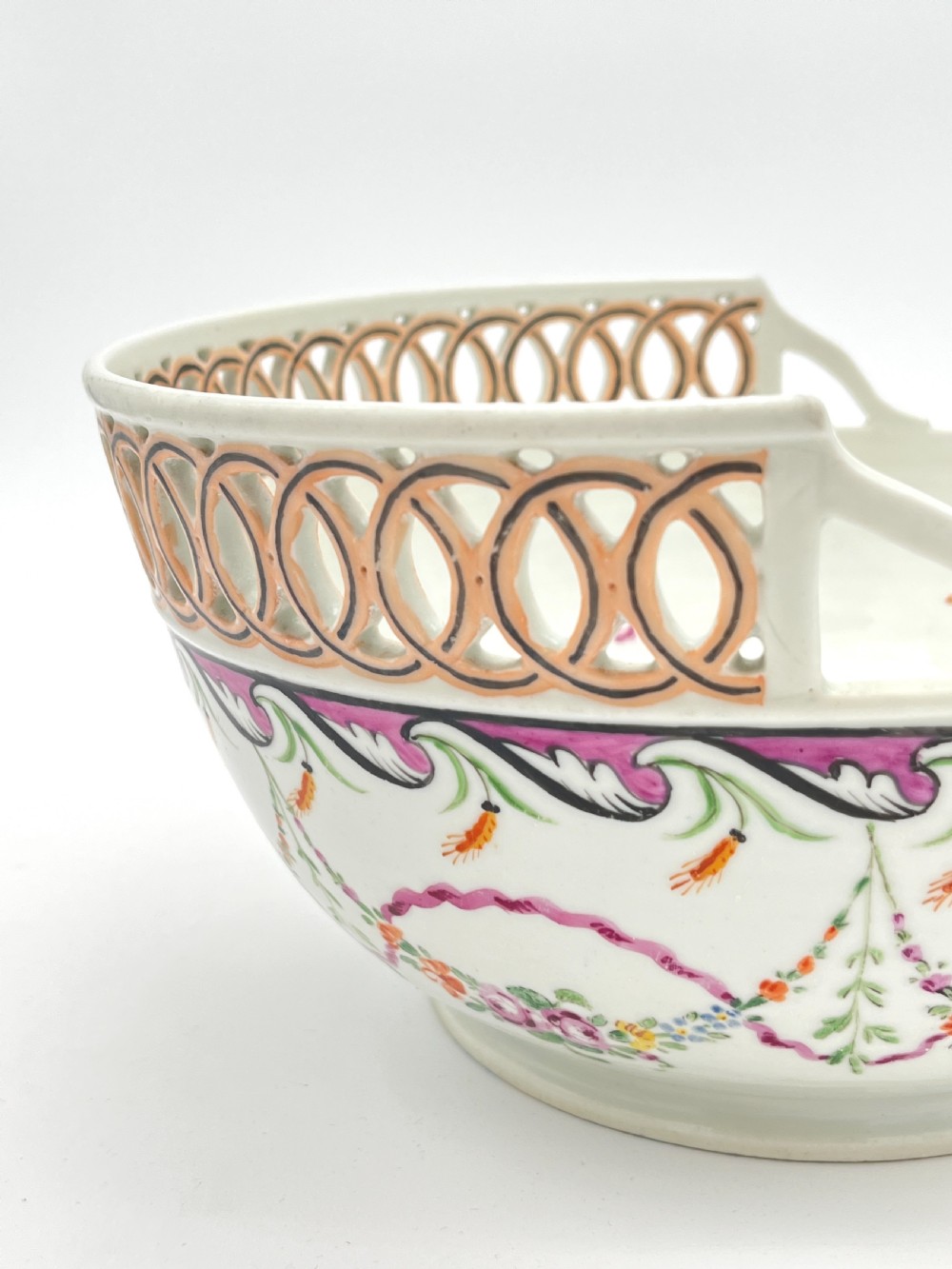 An eighteenth-century white porcelain punch bowl featuring a half-pierced reticulated gallery rim and hand-painted floral swags in pink, orange, and green. View II