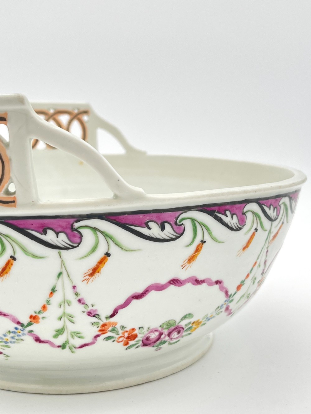 An eighteenth-century white porcelain punch bowl featuring a half-pierced reticulated gallery rim and hand-painted floral swags in pink, orange, and green. View III