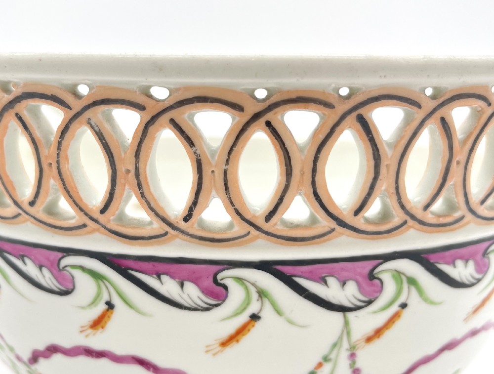 An eighteenth-century white porcelain punch bowl featuring a half-pierced reticulated gallery rim and hand-painted floral swags in pink, orange, and green. View VI