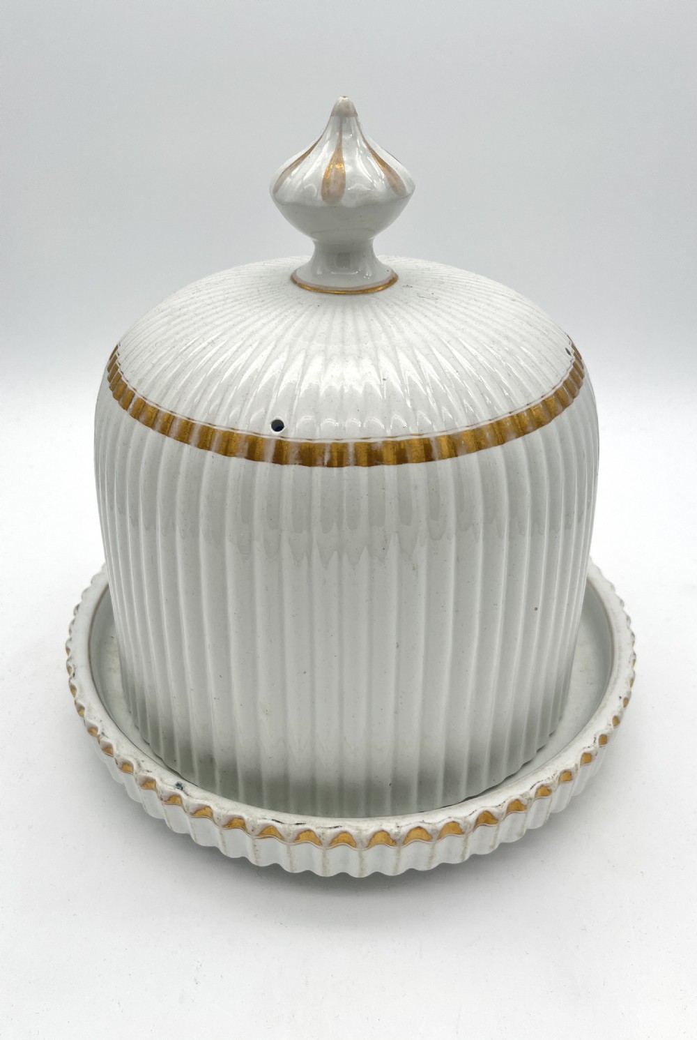A white ribbed ironstone cheese dome and matching stand featuring gilded accent bands and a moulded finial handle.