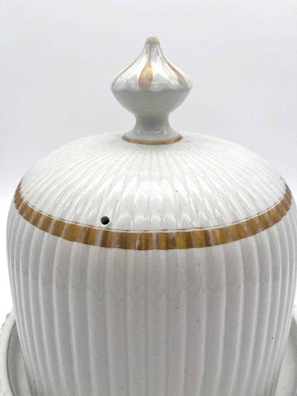 A white ribbed ironstone cheese dome and matching stand featuring gilded accent bands and a moulded finial handle. View II