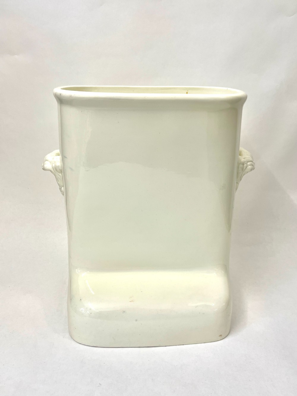 A cream-coloured glazed earthenware knee bath vessel with side handles and a stepped base profile.