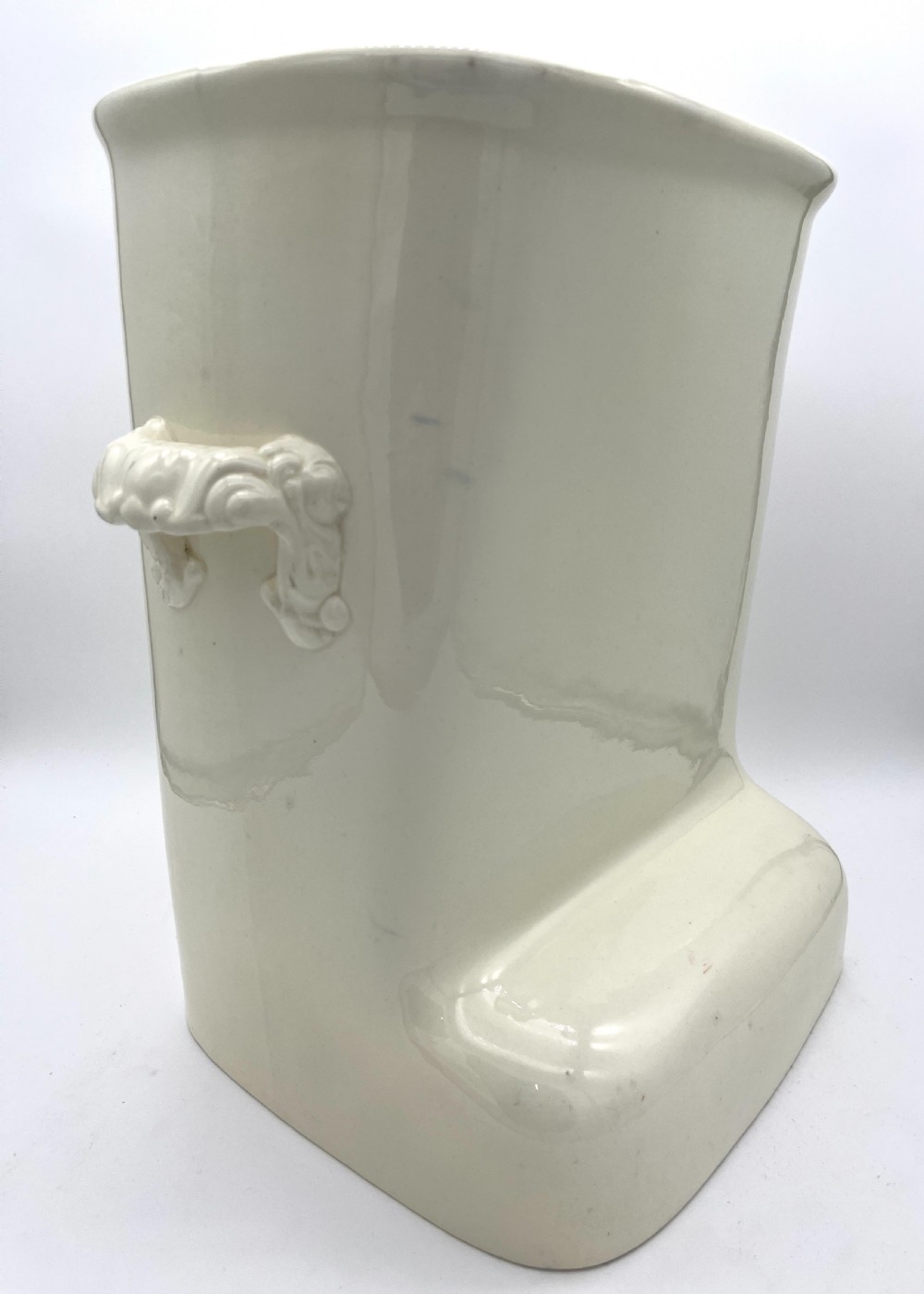 A cream-coloured glazed earthenware knee bath vessel with side handles and a stepped base profile. View II