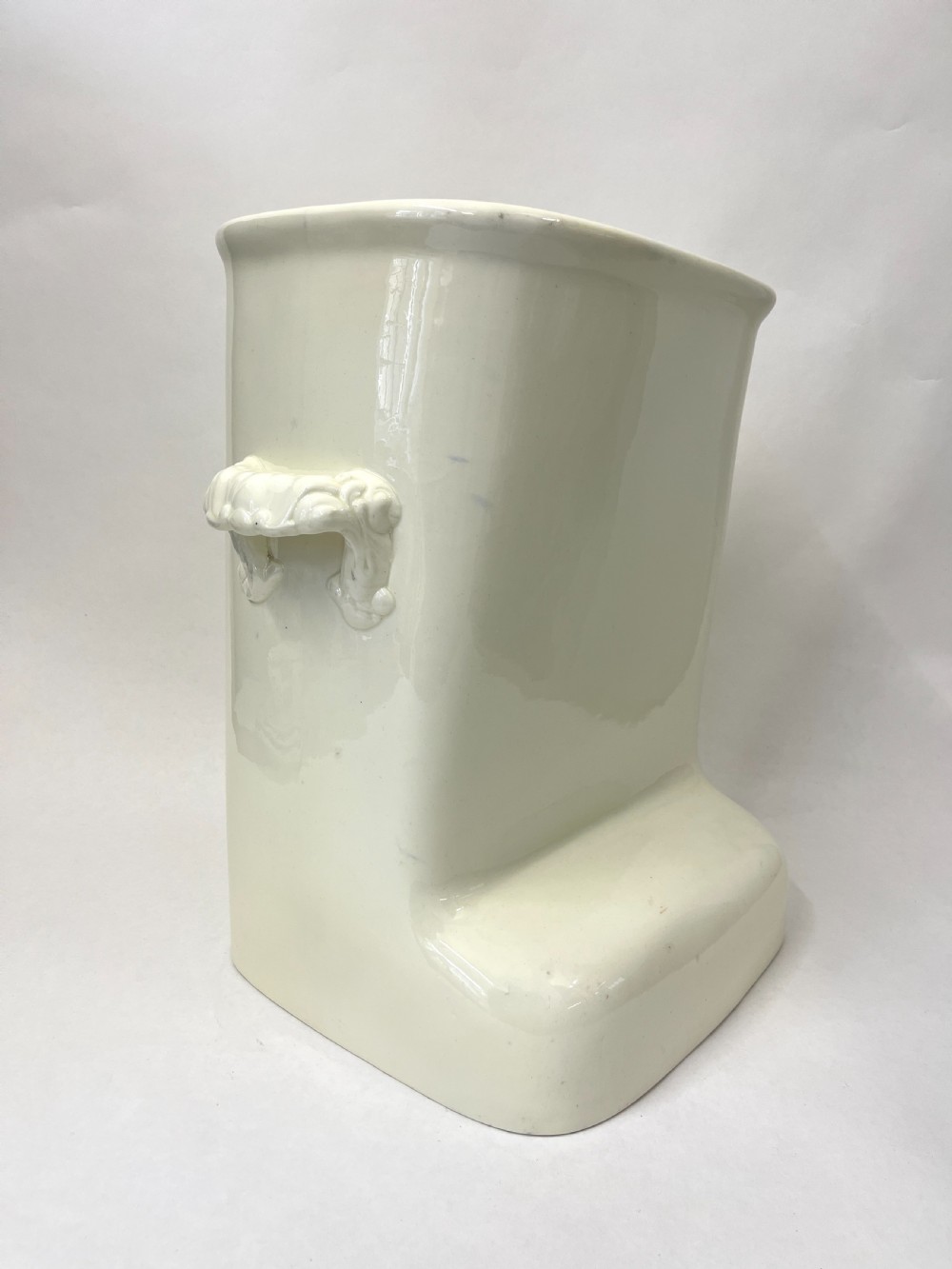 A cream-coloured glazed earthenware knee bath vessel with side handles and a stepped base profile. View III