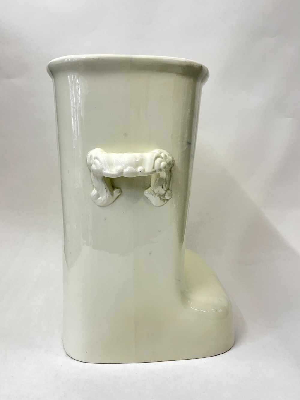 A cream-coloured glazed earthenware knee bath vessel with side handles and a stepped base profile. View V