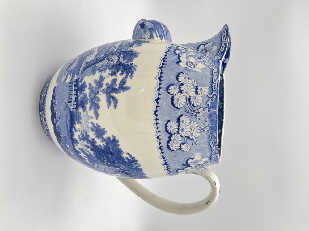 An antique blue and white earthenware footbath jug decorated with a floral upper band and a printed pastoral landscape scene. View III
