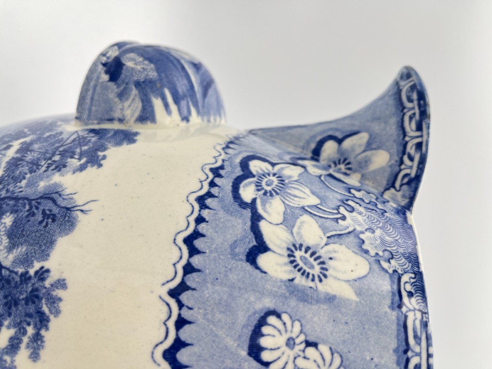 An antique blue and white earthenware footbath jug decorated with a floral upper band and a printed pastoral landscape scene. View V