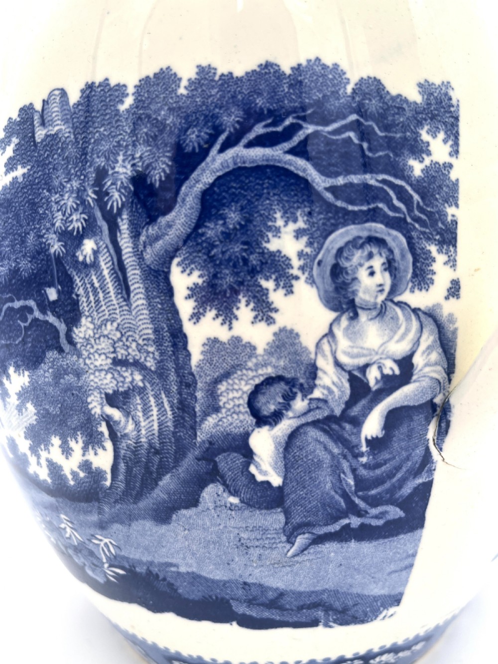 An antique blue and white earthenware footbath jug decorated with a floral upper band and a printed pastoral landscape scene. View VIII
