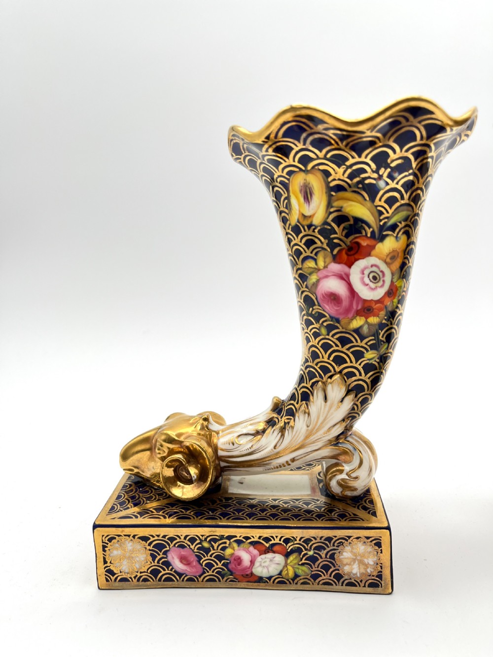 A pair of Regency porcelain cornucopia vases featuring deep cobalt blue fishscale patterning, gold leaf trim, and hand-painted floral panels on scroll bases. View II