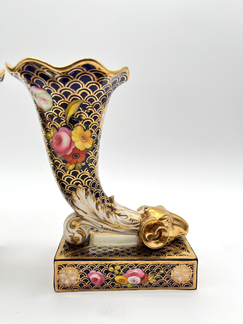 A pair of Regency porcelain cornucopia vases featuring deep cobalt blue fishscale patterning, gold leaf trim, and hand-painted floral panels on scroll bases. View III