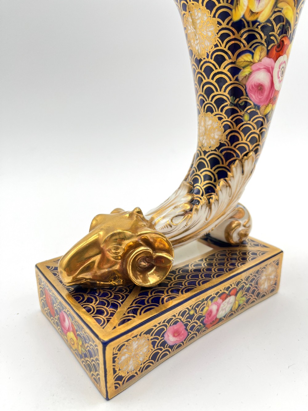 A pair of Regency porcelain cornucopia vases featuring deep cobalt blue fishscale patterning, gold leaf trim, and hand-painted floral panels on scroll bases. View IV