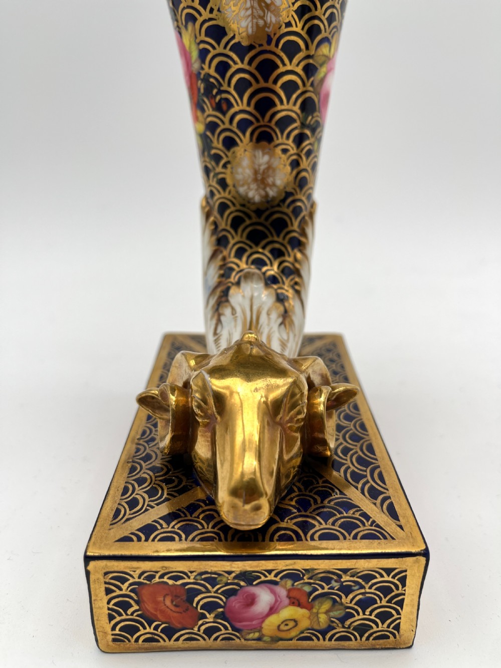 A pair of Regency porcelain cornucopia vases featuring deep cobalt blue fishscale patterning, gold leaf trim, and hand-painted floral panels on scroll bases. View V