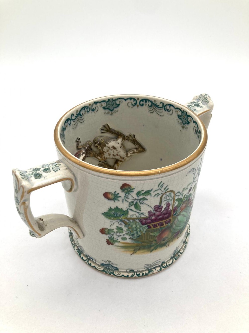 Victorian two-handled earthenware loving cup featuring a polychrome fruit basket illustration on the exterior and a moulded frog and newt attached to the interior wall.