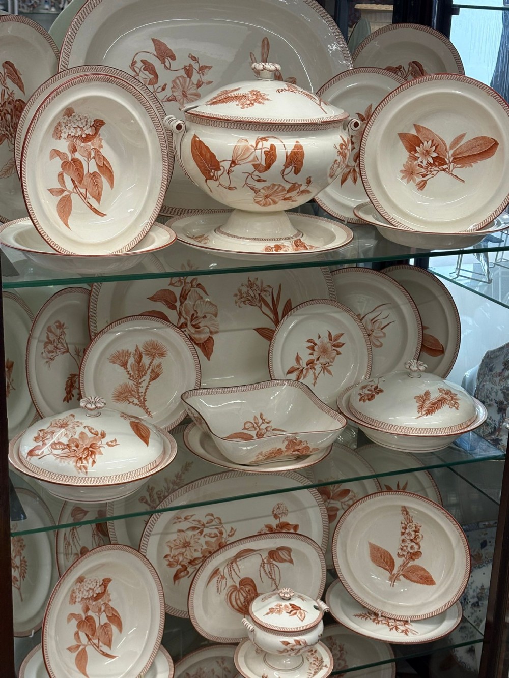 A Victorian Wedgwood creamware dinner service decorated with terracotta transfer-printed botanical motifs, including plates, platters, covered dishes, and a pedestal tureen.