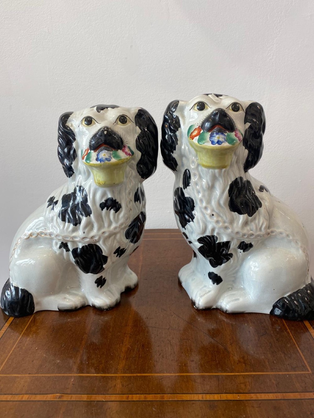 A matching pair of Victorian white earthenware Staffordshire spaniel figurines painted with black coat markings and holding baskets of flowers in their mouths.