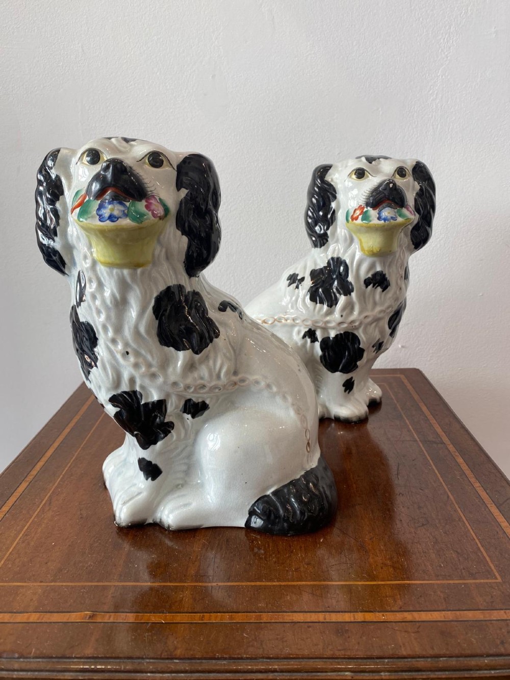 A matching pair of Victorian white earthenware Staffordshire spaniel figurines painted with black coat markings and holding baskets of flowers in their mouths. View II
