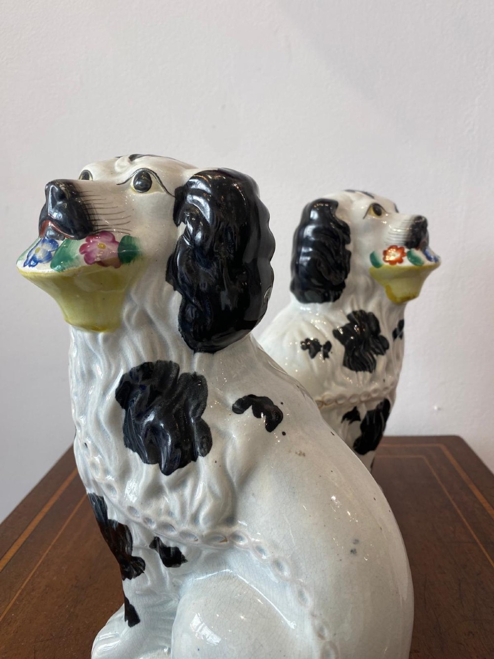A matching pair of Victorian white earthenware Staffordshire spaniel figurines painted with black coat markings and holding baskets of flowers in their mouths. View III