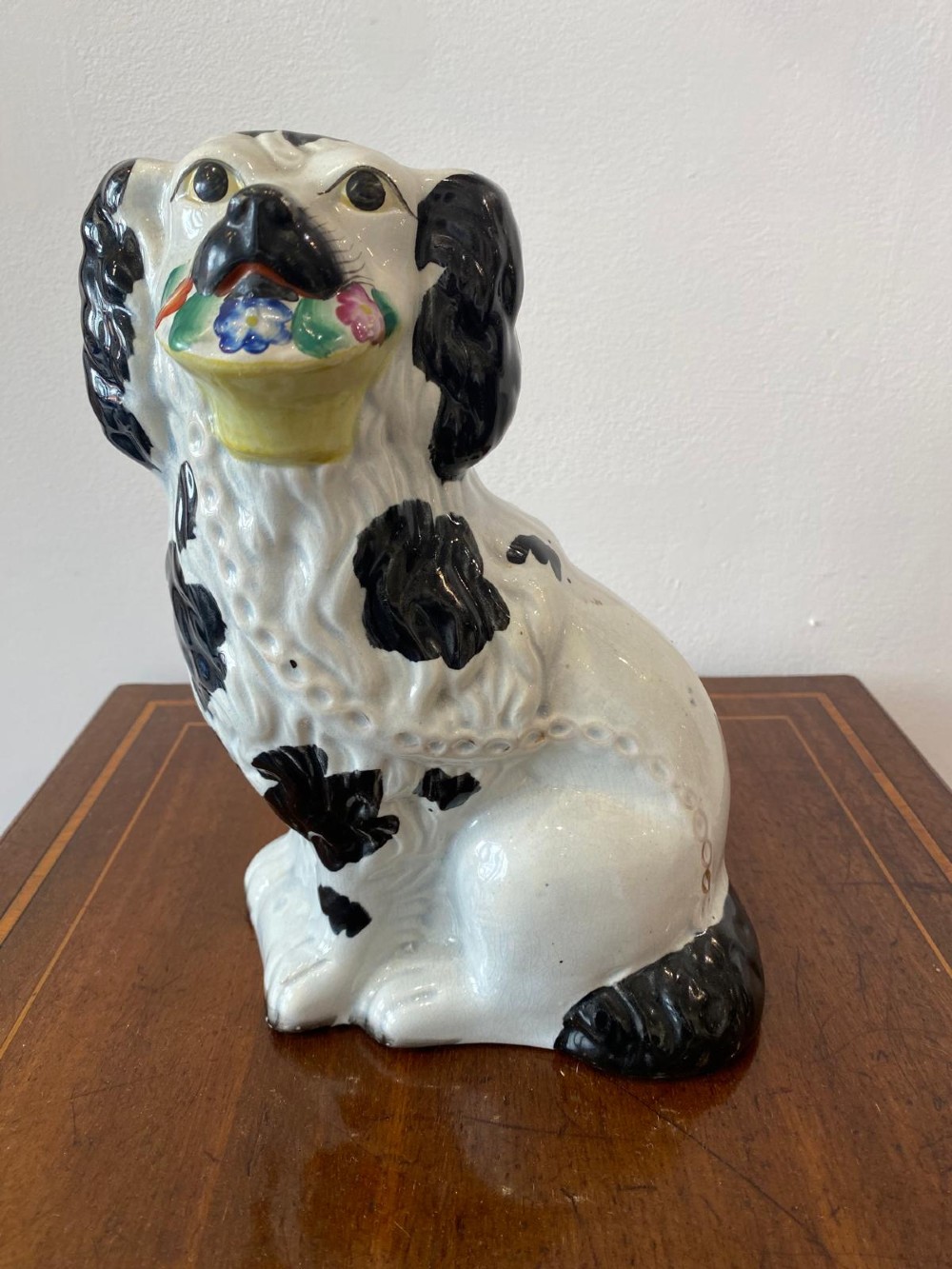 A matching pair of Victorian white earthenware Staffordshire spaniel figurines painted with black coat markings and holding baskets of flowers in their mouths. View IV