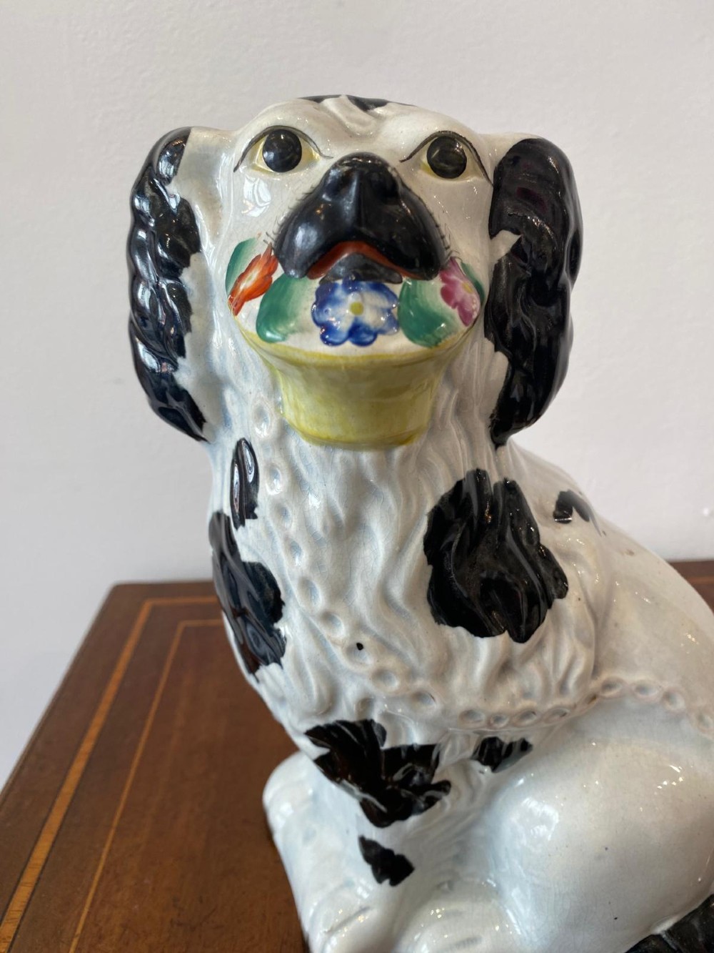 A matching pair of Victorian white earthenware Staffordshire spaniel figurines painted with black coat markings and holding baskets of flowers in their mouths. View V