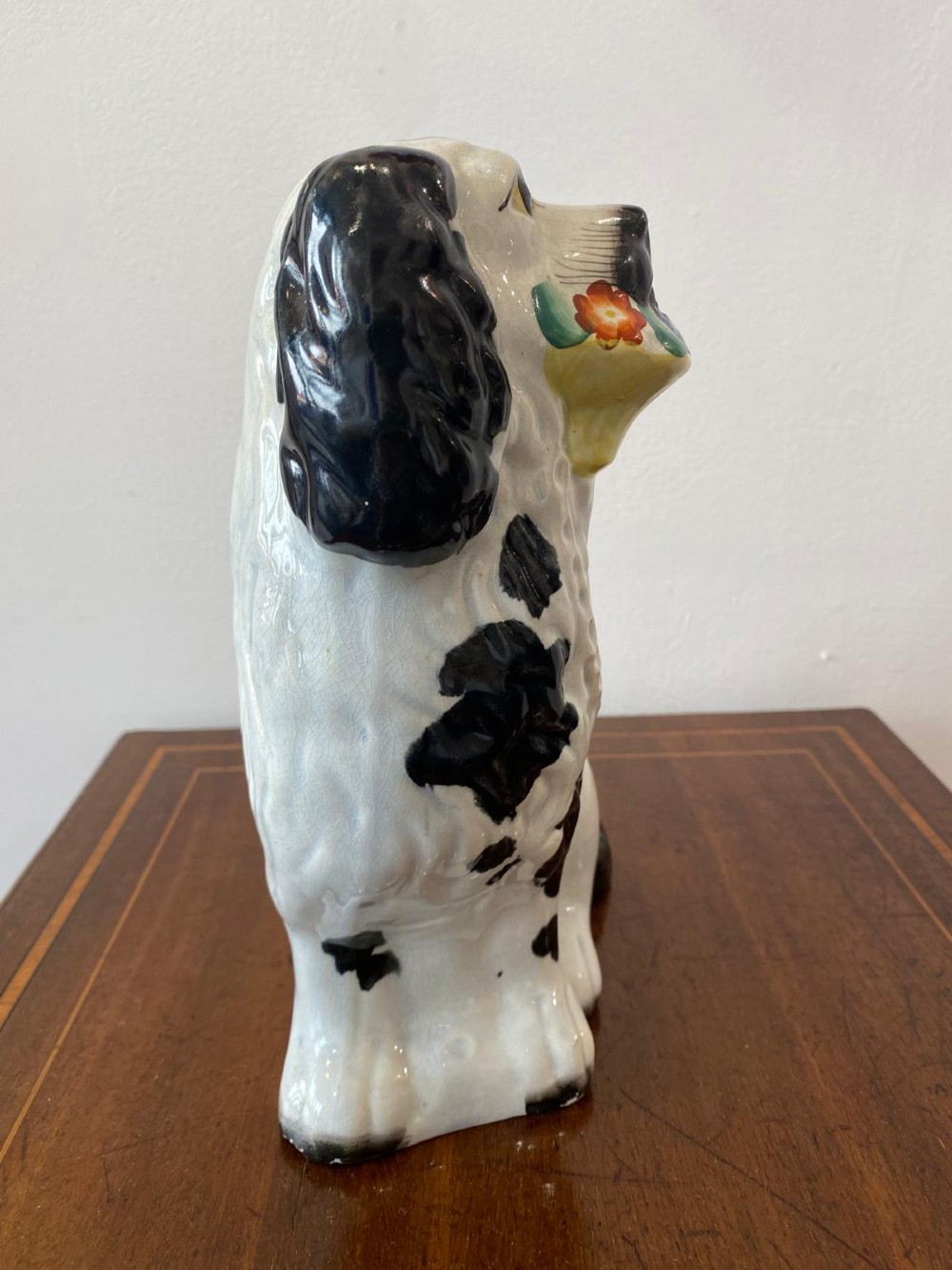 A matching pair of Victorian white earthenware Staffordshire spaniel figurines painted with black coat markings and holding baskets of flowers in their mouths. View VI