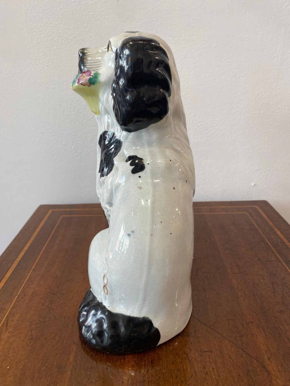 A matching pair of Victorian white earthenware Staffordshire spaniel figurines painted with black coat markings and holding baskets of flowers in their mouths. View VIII