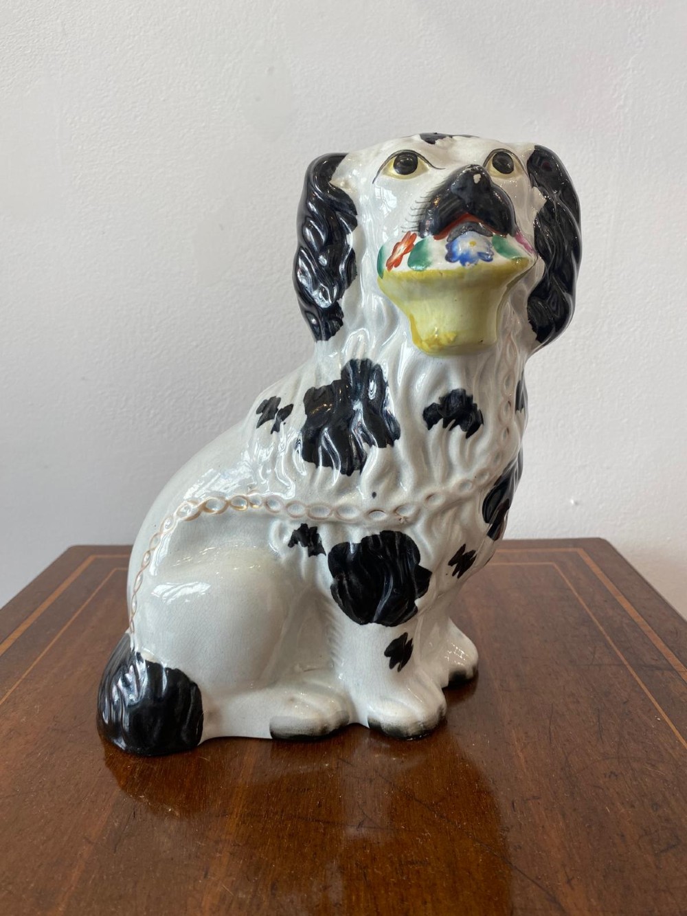 A matching pair of Victorian white earthenware Staffordshire spaniel figurines painted with black coat markings and holding baskets of flowers in their mouths. View X