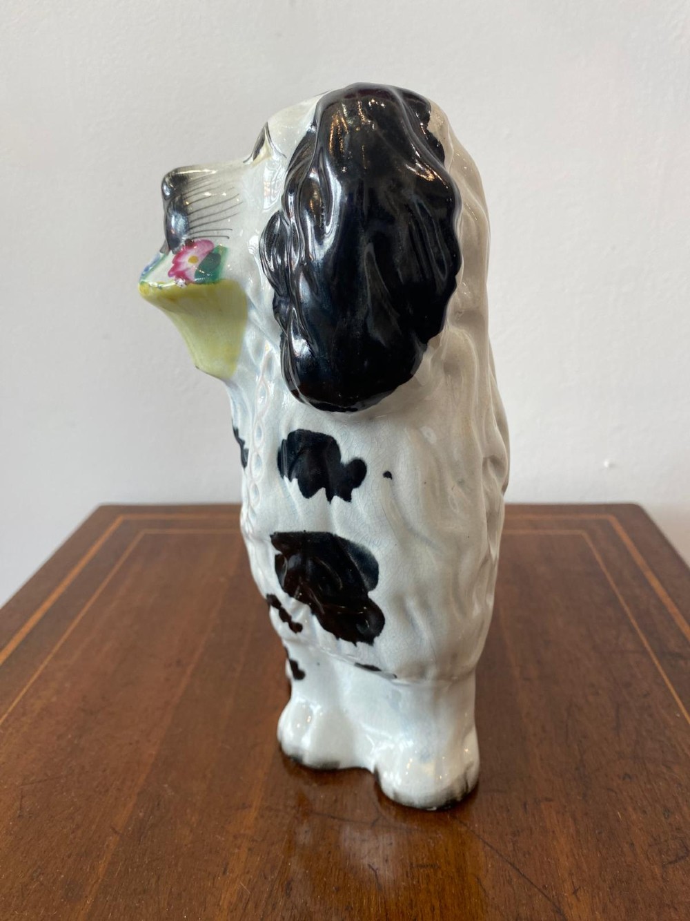 A matching pair of Victorian white earthenware Staffordshire spaniel figurines painted with black coat markings and holding baskets of flowers in their mouths. View XII