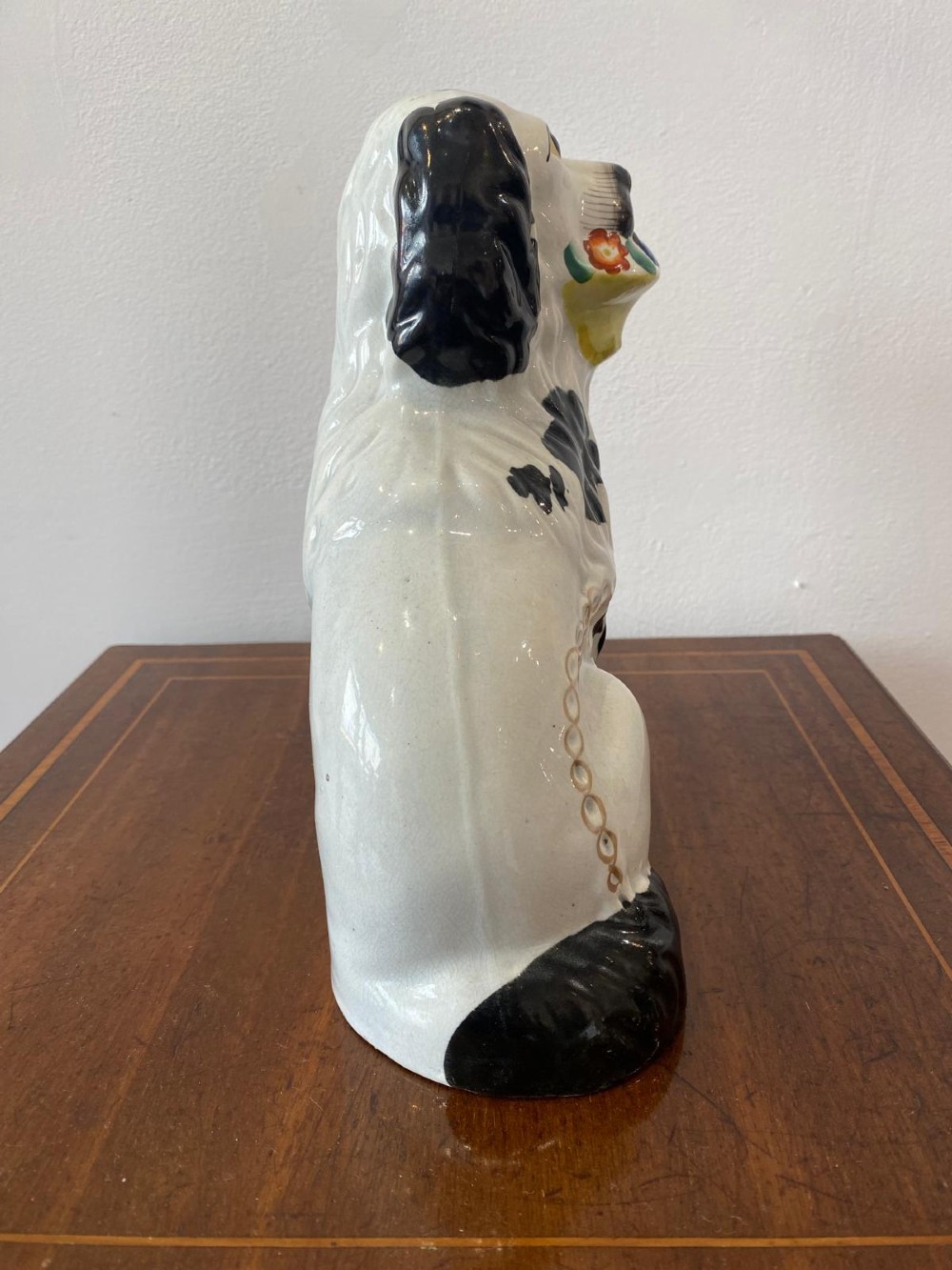 A matching pair of Victorian white earthenware Staffordshire spaniel figurines painted with black coat markings and holding baskets of flowers in their mouths. View XIV