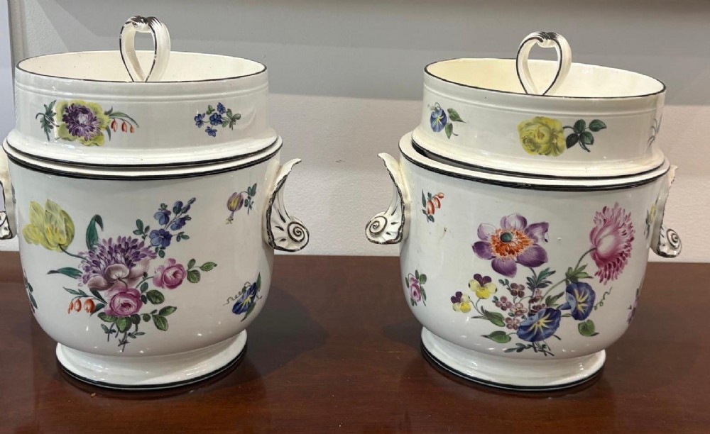 A pair of Georgian creamware ice pails decorated with hand-painted botanical flowers, featuring side scroll handles and tiered lids.